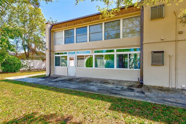 rear view of property with stucco siding, a yard, and fence