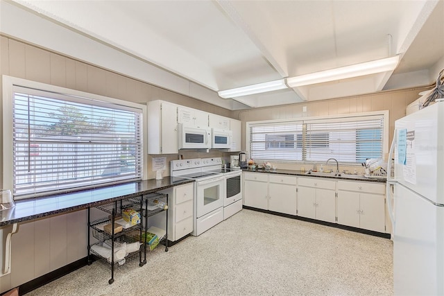 kitchen featuring dark countertops, wood walls, white appliances, white cabinetry, and a sink