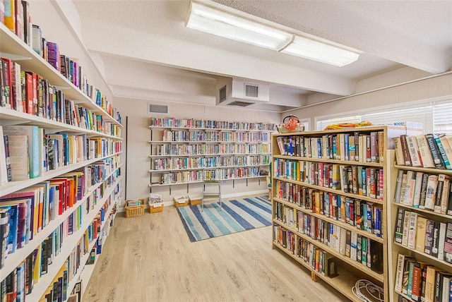 sitting room featuring wood finished floors, visible vents, baseboards, wall of books, and beamed ceiling