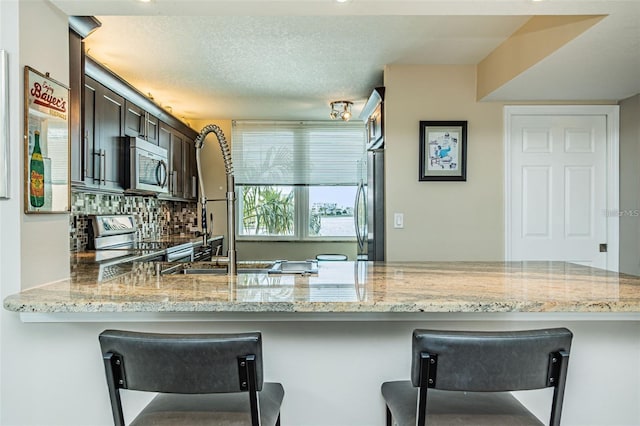 kitchen with light stone counters, stainless steel appliances, dark brown cabinetry, and built in study area