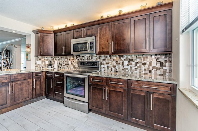 kitchen with decorative backsplash, dark brown cabinetry, light stone countertops, and stainless steel appliances