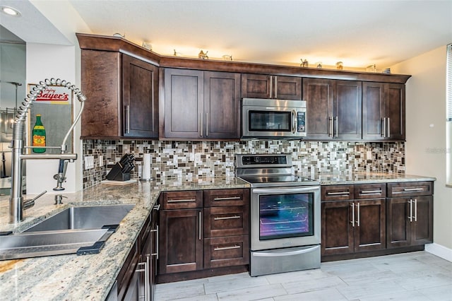 kitchen with dark brown cabinetry, decorative backsplash, appliances with stainless steel finishes, and light stone counters