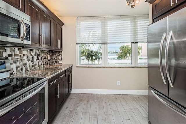 kitchen with light wood-style flooring, stone countertops, stainless steel appliances, dark brown cabinetry, and tasteful backsplash