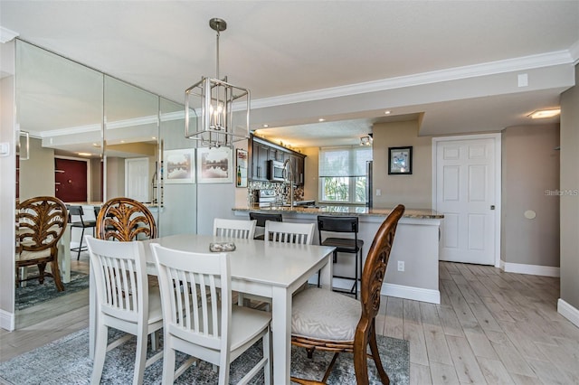 dining space with light wood-type flooring, baseboards, a chandelier, and crown molding