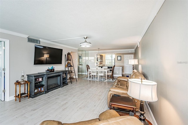 living room with visible vents, a textured ceiling, crown molding, light wood finished floors, and baseboards