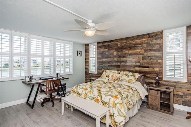 bedroom with wooden walls, multiple windows, a textured ceiling, and wood finished floors