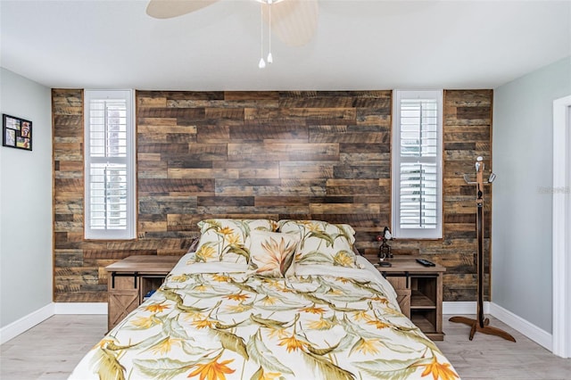 bedroom with wood walls, an accent wall, baseboards, and wood finished floors