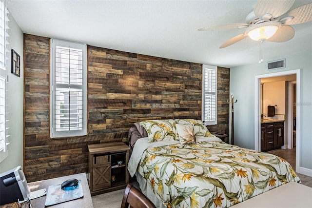 bedroom with visible vents, a ceiling fan, wooden walls, and wood finished floors