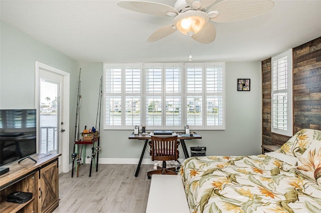 bedroom with multiple windows, baseboards, light wood-type flooring, and wood walls