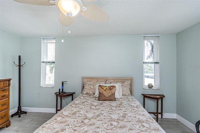 bedroom featuring ceiling fan, baseboards, a textured ceiling, and wood finished floors