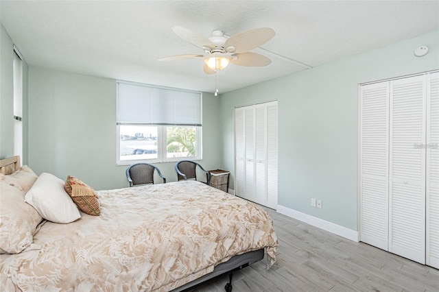 bedroom with ceiling fan, two closets, baseboards, and wood finished floors