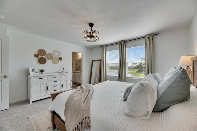 bedroom featuring baseboards, light colored carpet, a notable chandelier, a textured ceiling, and ensuite bath