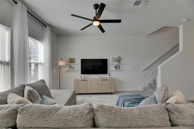 living room featuring visible vents, baseboards, stairway, light carpet, and a ceiling fan