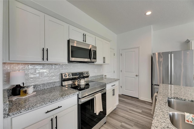 kitchen with light stone counters, tasteful backsplash, appliances with stainless steel finishes, and light wood finished floors