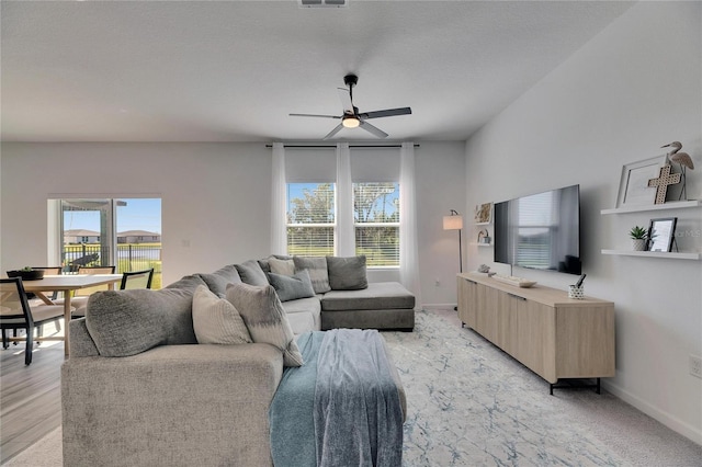 living room featuring light wood-style floors, visible vents, a ceiling fan, and baseboards