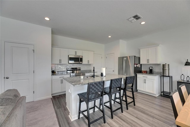 kitchen with visible vents, a breakfast bar area, white cabinets, stainless steel appliances, and a sink