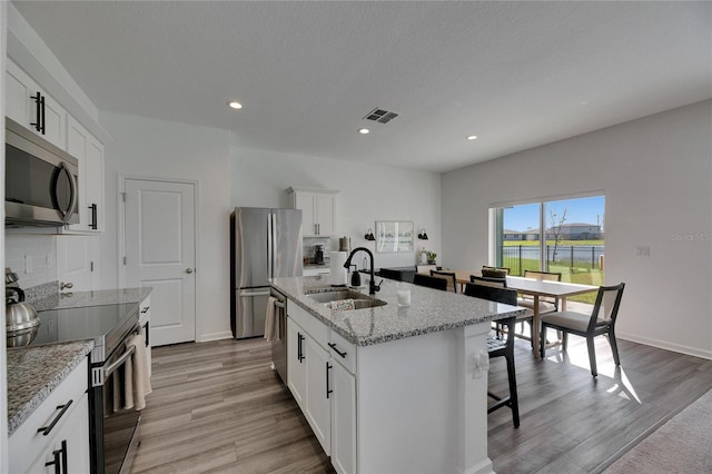 kitchen with visible vents, a sink, a kitchen breakfast bar, stainless steel appliances, and a kitchen island with sink