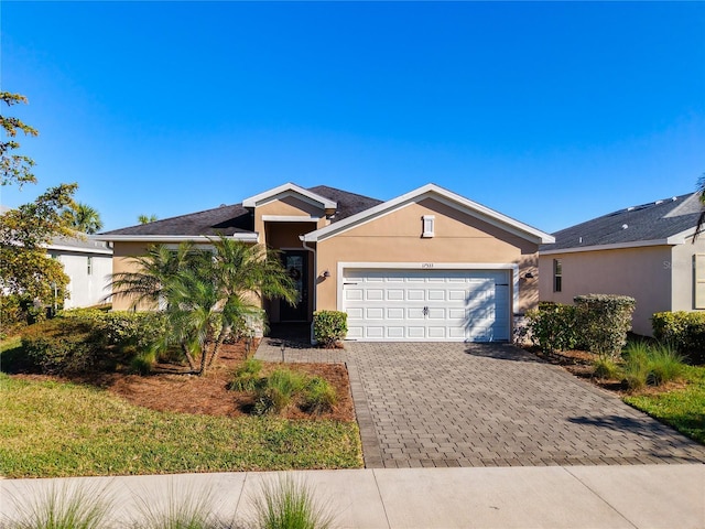 ranch-style home with stucco siding, an attached garage, and decorative driveway