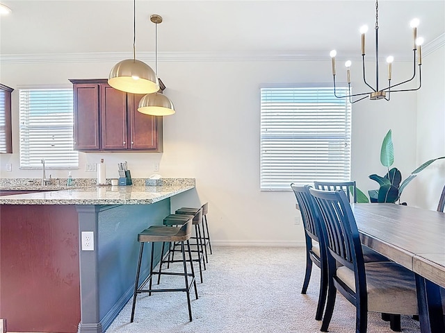 kitchen featuring light stone counters, a breakfast bar, ornamental molding, hanging light fixtures, and light colored carpet