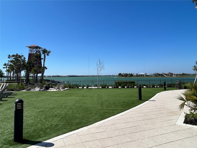 view of property's community with a water view, fence, and a lawn