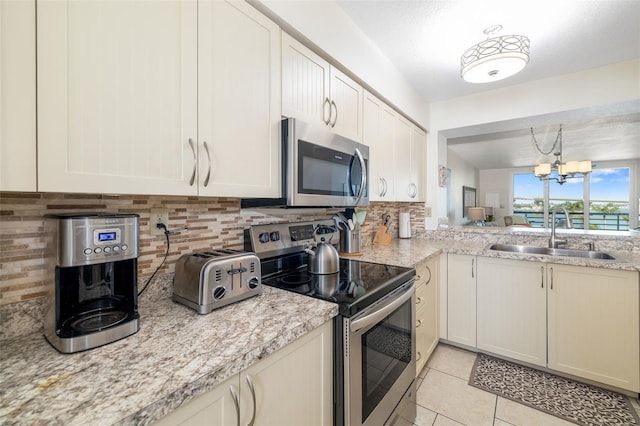 kitchen with light tile patterned floors, a sink, appliances with stainless steel finishes, backsplash, and a chandelier