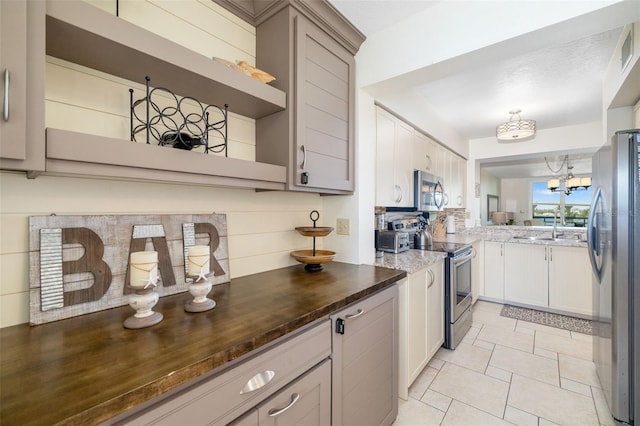 kitchen with open shelves, dark stone counters, a sink, stainless steel appliances, and a notable chandelier