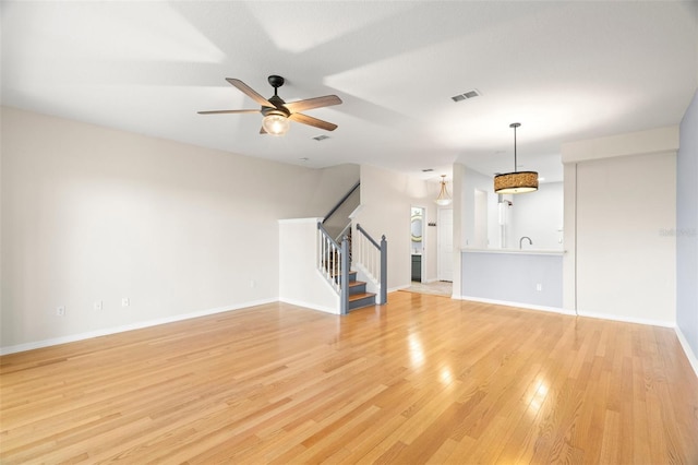 unfurnished living room featuring stairway, a ceiling fan, visible vents, light wood finished floors, and baseboards