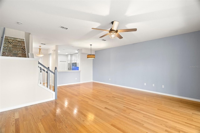 unfurnished living room featuring a ceiling fan, visible vents, baseboards, stairs, and light wood-style floors