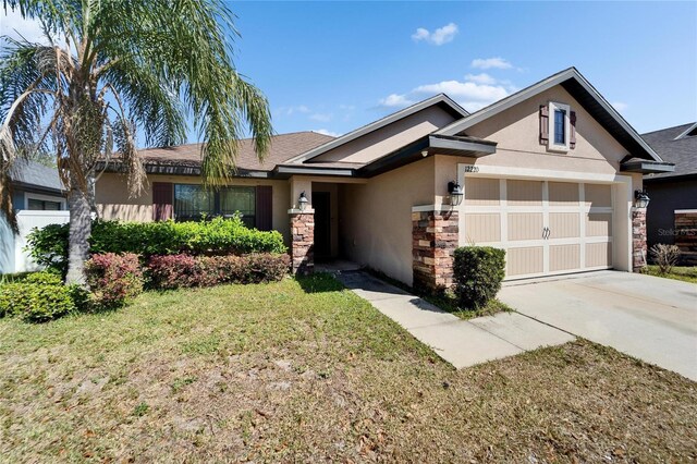 view of front of home with stucco siding, driveway, stone siding, a front yard, and a garage