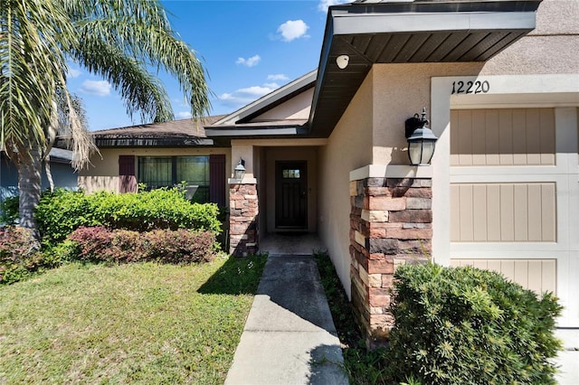 doorway to property featuring stucco siding, stone siding, and a lawn