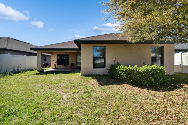 rear view of house featuring a yard, fence, and stucco siding