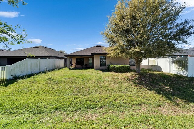 rear view of house featuring a fenced backyard, stucco siding, and a yard