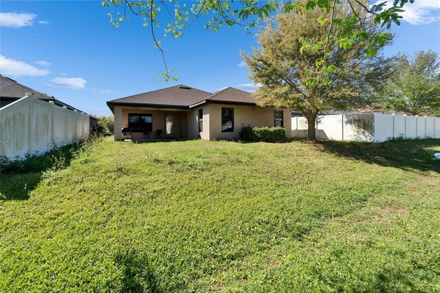 rear view of property with a yard, fence private yard, and stucco siding