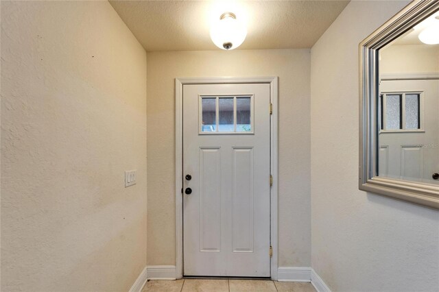 doorway featuring light tile patterned floors, baseboards, and a textured ceiling