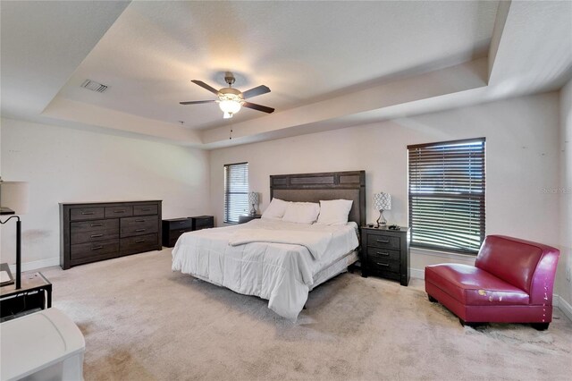 carpeted bedroom featuring visible vents, multiple windows, a raised ceiling, and baseboards