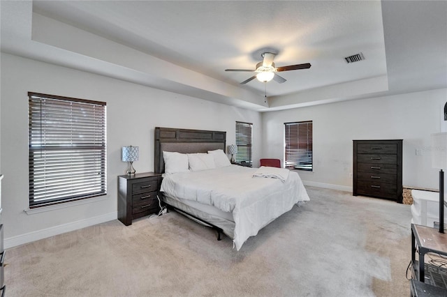 bedroom with baseboards, visible vents, a raised ceiling, and light carpet