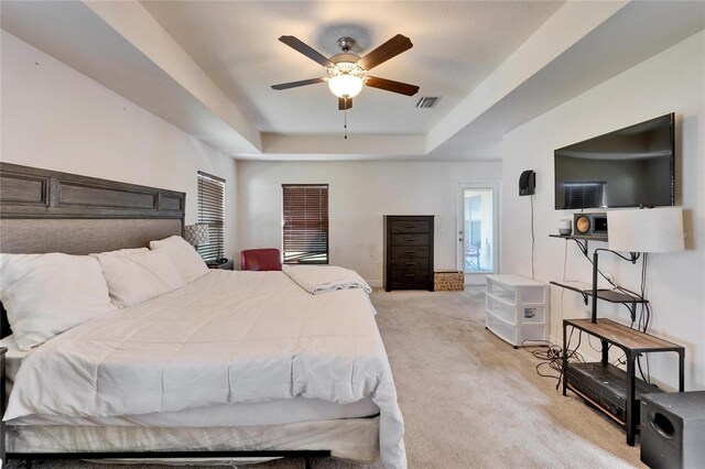 bedroom featuring visible vents, light colored carpet, a tray ceiling, and ceiling fan