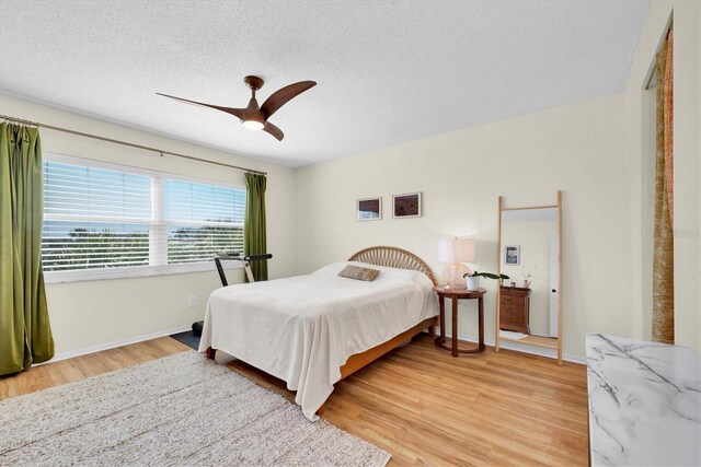 bedroom featuring baseboards, light wood-style floors, a ceiling fan, and a textured ceiling