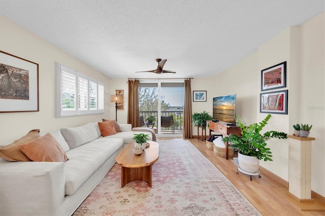 living area featuring baseboards, a textured ceiling, light wood-style flooring, and a ceiling fan