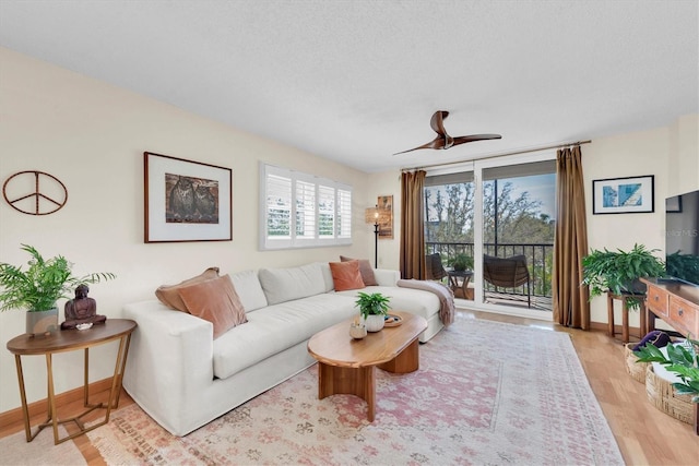 living area with baseboards, a textured ceiling, a ceiling fan, and light wood finished floors