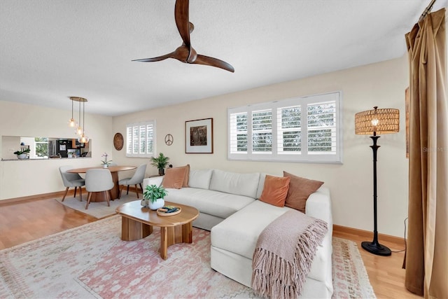 living room with a textured ceiling, light wood finished floors, and ceiling fan