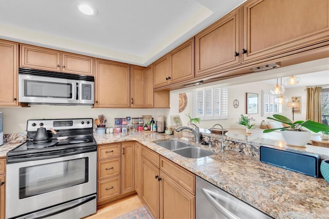 kitchen with light stone counters, light wood-style flooring, stainless steel appliances, and a sink