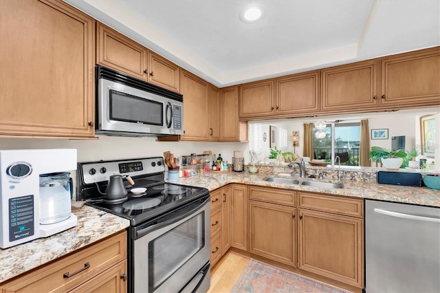 kitchen featuring light stone countertops, a sink, stainless steel appliances, light wood-style floors, and brown cabinets