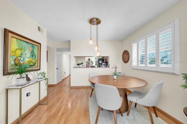 dining room with baseboards, visible vents, light wood-type flooring, and a textured ceiling