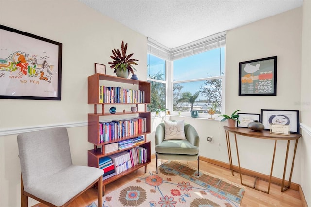 living area featuring a textured ceiling, a wall of windows, baseboards, and wood finished floors