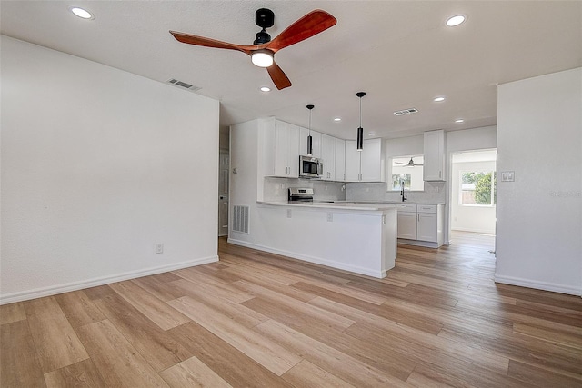 kitchen with visible vents, light wood-style flooring, stainless steel microwave, light countertops, and decorative backsplash