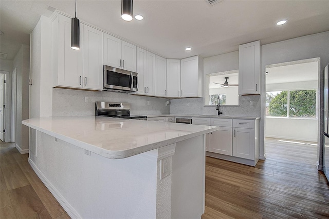 kitchen featuring wood finished floors, a peninsula, a sink, appliances with stainless steel finishes, and white cabinetry