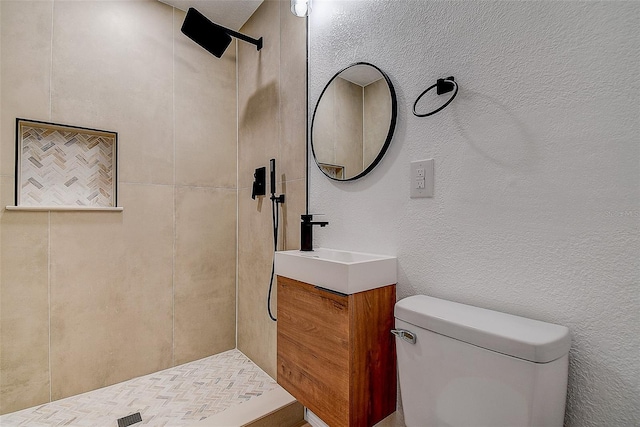 bathroom featuring a textured wall, toilet, vanity, and a tile shower