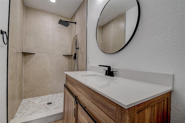 bathroom with tiled shower, vanity, and a textured wall