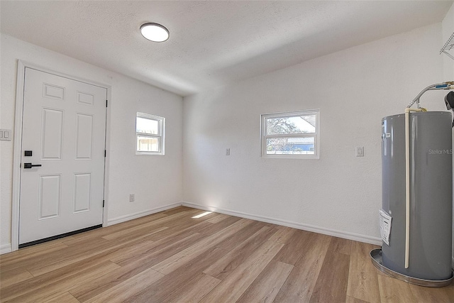 foyer entrance with baseboards, water heater, light wood finished floors, and a textured ceiling